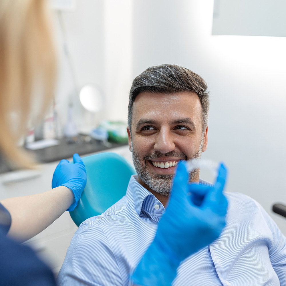 A man receiving dental care with a smile on his face, sitting in a chair while a dental professional works on him.
